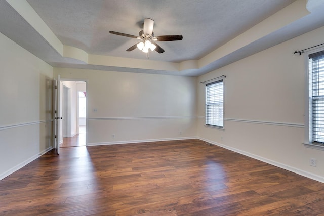 spare room with a textured ceiling, dark hardwood / wood-style flooring, a tray ceiling, and ceiling fan