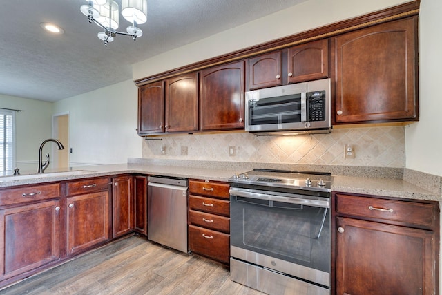 kitchen featuring appliances with stainless steel finishes, light stone counters, sink, light hardwood / wood-style flooring, and a chandelier