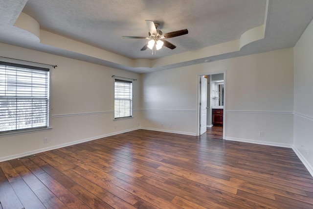 unfurnished room featuring a tray ceiling, ceiling fan, dark hardwood / wood-style flooring, and a textured ceiling