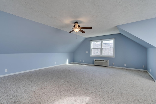 additional living space featuring a wall mounted air conditioner, vaulted ceiling, carpet flooring, ceiling fan, and a textured ceiling