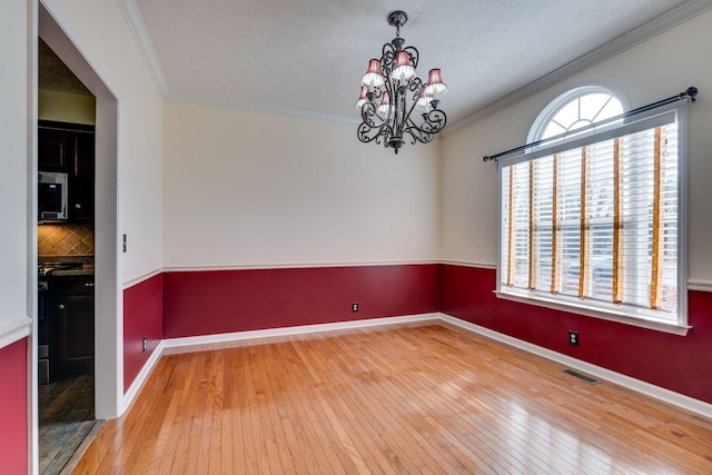 empty room featuring a textured ceiling, hardwood / wood-style flooring, crown molding, and a notable chandelier