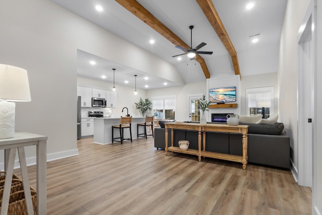 living room featuring sink, ceiling fan, beamed ceiling, plenty of natural light, and light hardwood / wood-style floors