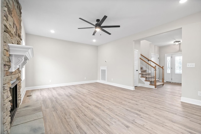 unfurnished living room with light hardwood / wood-style floors, a stone fireplace, and ceiling fan