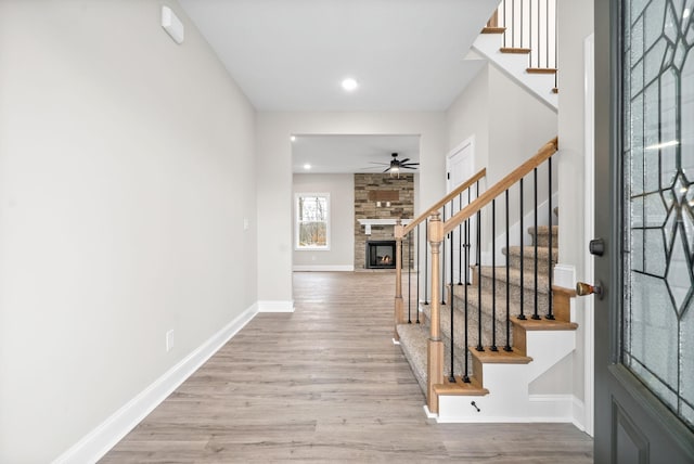 foyer entrance with a large fireplace, baseboards, stairway, and wood finished floors