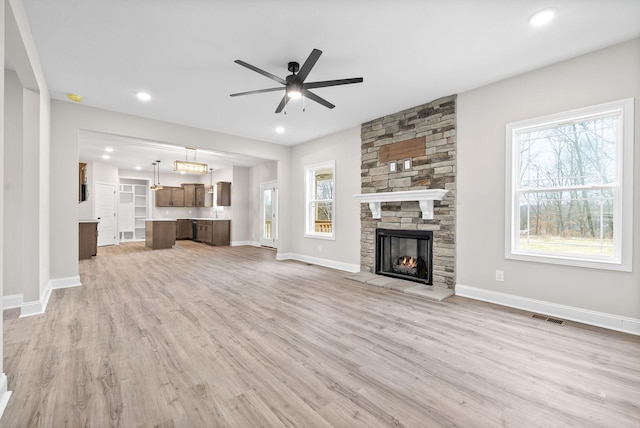 unfurnished living room featuring a stone fireplace, visible vents, baseboards, a ceiling fan, and light wood-type flooring