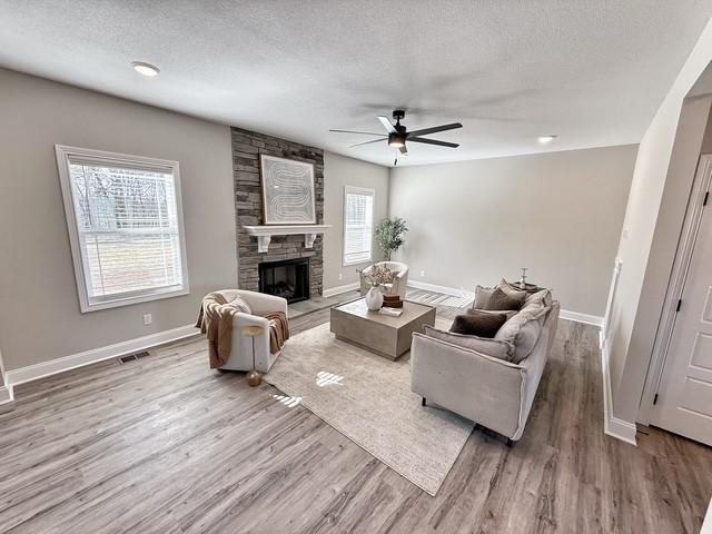 living area featuring visible vents, a stone fireplace, a textured ceiling, wood finished floors, and baseboards