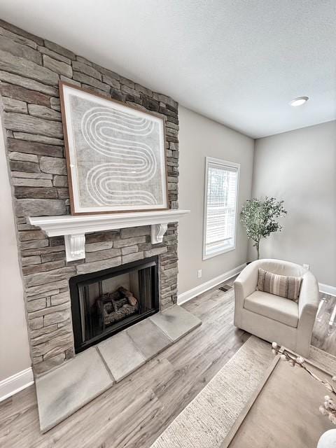 living room featuring a stone fireplace, baseboards, and wood finished floors