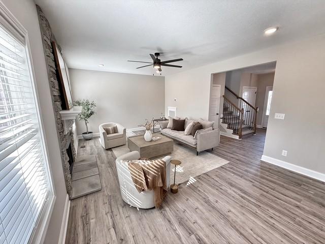 living area with ceiling fan, a fireplace, wood finished floors, baseboards, and stairs