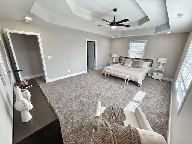 bedroom with carpet floors, a tray ceiling, visible vents, and multiple windows