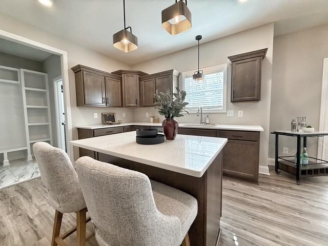 kitchen featuring dark brown cabinetry, pendant lighting, light countertops, and a sink