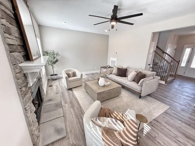 living area with a fireplace, wood finished floors, a ceiling fan, baseboards, and stairs