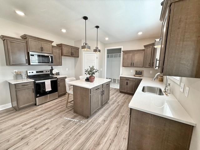 kitchen featuring light wood-style floors, a kitchen island, appliances with stainless steel finishes, and a sink