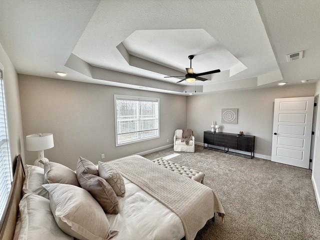 carpeted bedroom with a raised ceiling, visible vents, ceiling fan, and baseboards