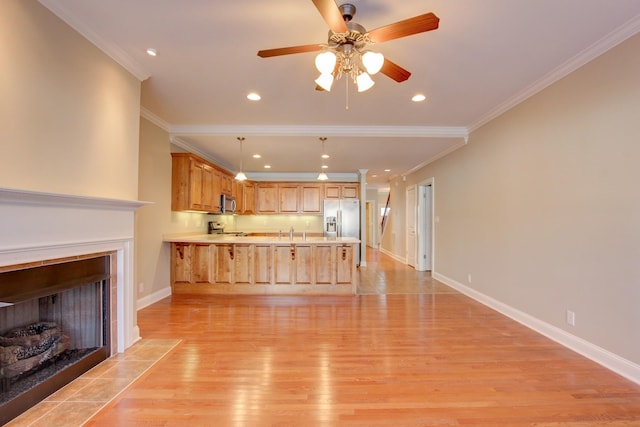 interior space featuring kitchen peninsula, light brown cabinetry, appliances with stainless steel finishes, and ornamental molding