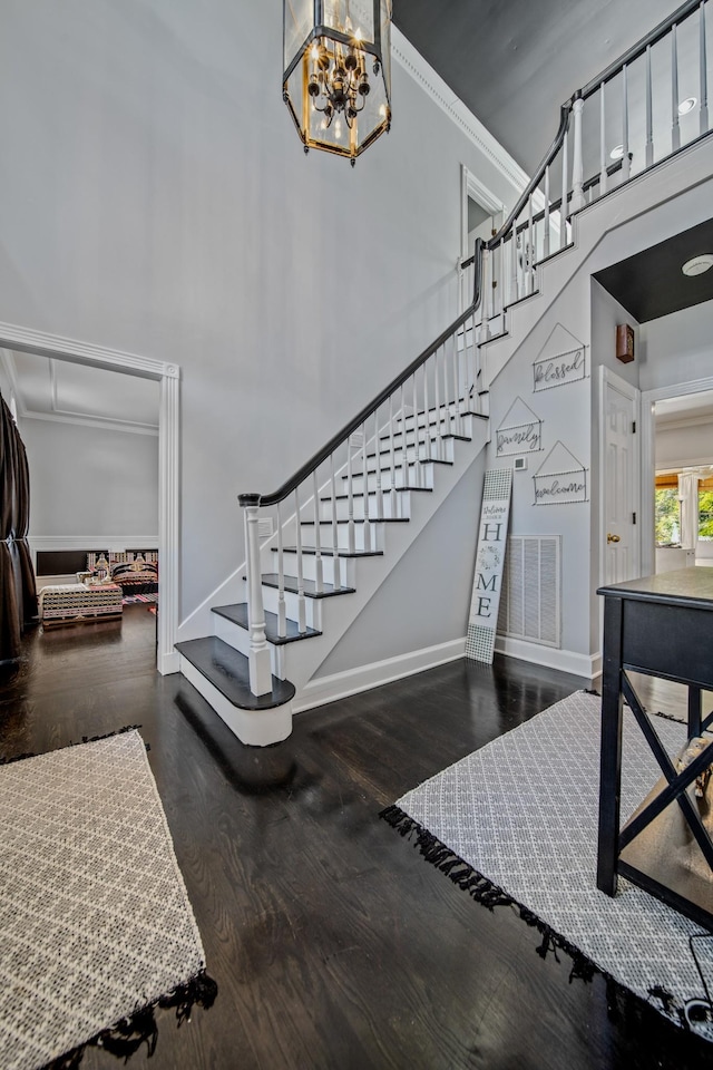 stairway featuring a high ceiling, hardwood / wood-style flooring, an inviting chandelier, and ornamental molding