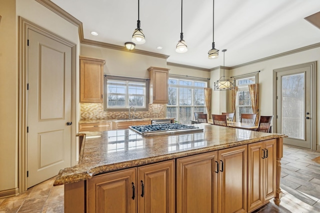 kitchen featuring sink, hanging light fixtures, light stone counters, stainless steel gas stovetop, and a kitchen island