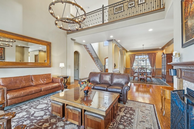 living room with a notable chandelier, wood-type flooring, ornamental molding, and a high ceiling