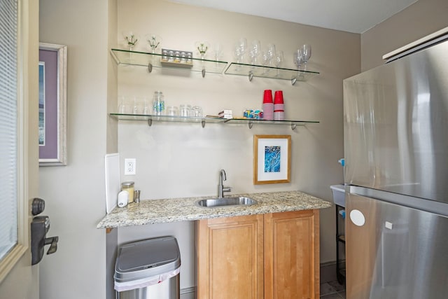 bar featuring stainless steel fridge, light stone counters, and sink