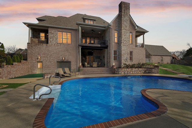 pool at dusk featuring ceiling fan and a patio area