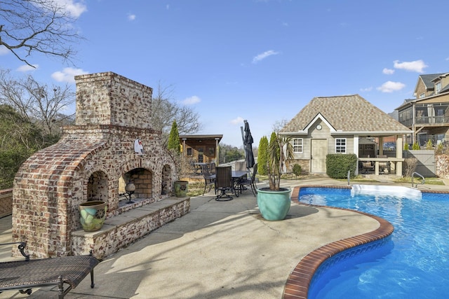 view of pool featuring an outdoor stone fireplace, a patio area, and an outbuilding