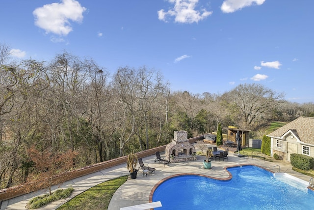 view of pool featuring an outdoor stone fireplace, a diving board, and a patio