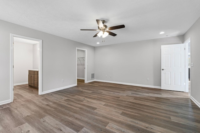 unfurnished bedroom featuring a walk in closet, a closet, ceiling fan, and dark hardwood / wood-style floors