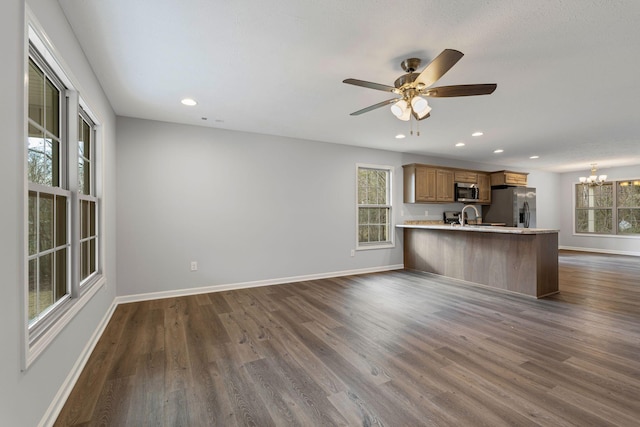 kitchen featuring ceiling fan with notable chandelier, dark hardwood / wood-style floors, appliances with stainless steel finishes, kitchen peninsula, and a breakfast bar area