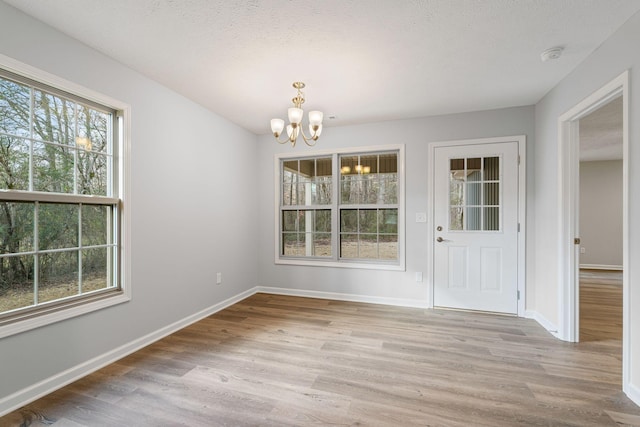 unfurnished dining area with a textured ceiling, light wood-type flooring, and a notable chandelier