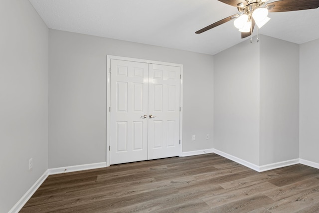 unfurnished bedroom with ceiling fan, dark wood-type flooring, and a closet