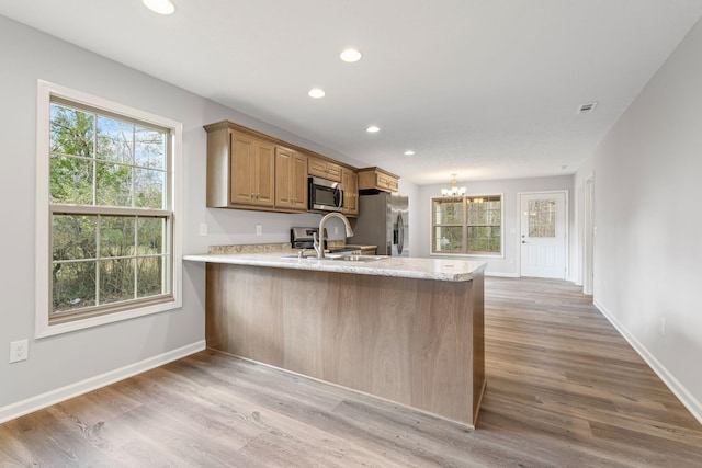 kitchen with sink, light hardwood / wood-style flooring, a notable chandelier, kitchen peninsula, and stainless steel appliances