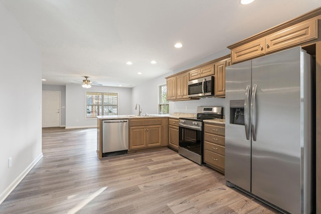 kitchen with kitchen peninsula, appliances with stainless steel finishes, light wood-type flooring, ceiling fan, and sink