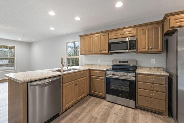 kitchen with kitchen peninsula, appliances with stainless steel finishes, light hardwood / wood-style floors, and sink