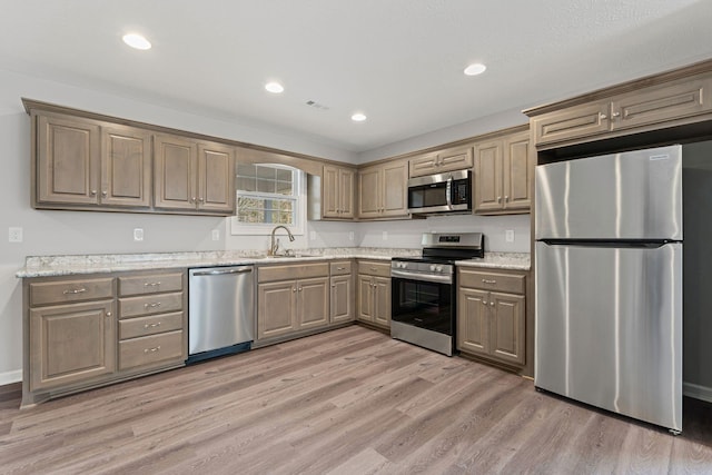 kitchen featuring light hardwood / wood-style floors, light stone counters, sink, and appliances with stainless steel finishes