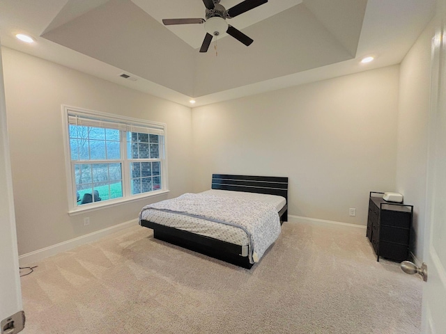 bedroom featuring a raised ceiling, light colored carpet, and ceiling fan