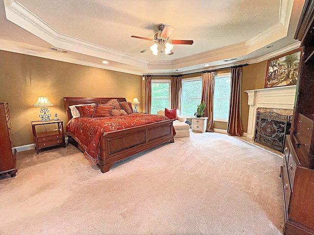 bedroom with a high end fireplace, ornamental molding, a tray ceiling, light colored carpet, and ceiling fan