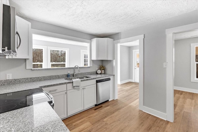 kitchen with white cabinets, appliances with stainless steel finishes, light wood-style floors, and a sink