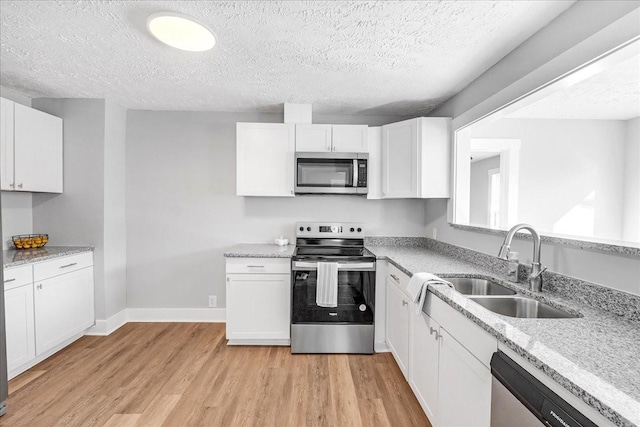 kitchen with light stone counters, light wood-style flooring, appliances with stainless steel finishes, white cabinetry, and a sink