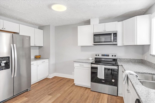 kitchen featuring light wood finished floors, white cabinetry, baseboards, stainless steel appliances, and a textured ceiling