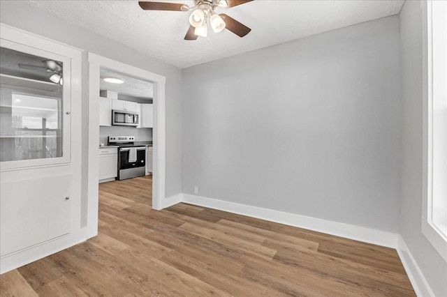 spare room with ceiling fan, light wood-style flooring, baseboards, and a textured ceiling