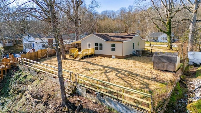 back of house with a storage unit, a wooden deck, an outdoor structure, and a fenced backyard