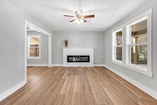 unfurnished living room with baseboards, a glass covered fireplace, a textured ceiling, and light wood-style floors