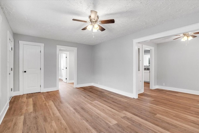 empty room with baseboards, a textured ceiling, light wood-type flooring, and a ceiling fan