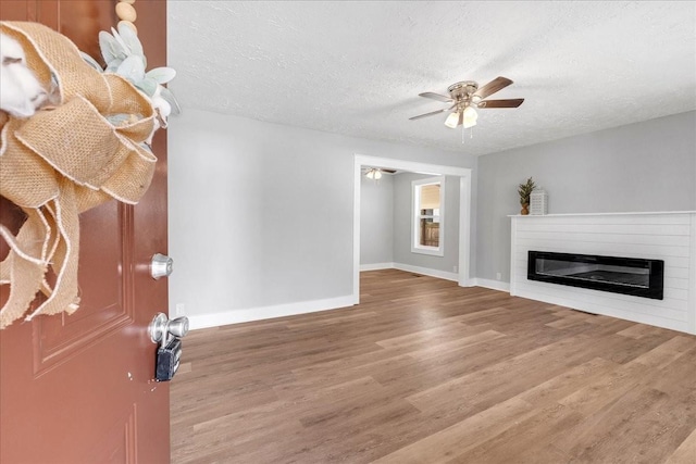 unfurnished living room featuring a glass covered fireplace, a textured ceiling, ceiling fan, and wood finished floors