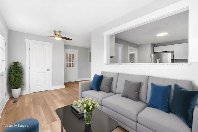 living room featuring visible vents, baseboards, light wood-type flooring, and ceiling fan