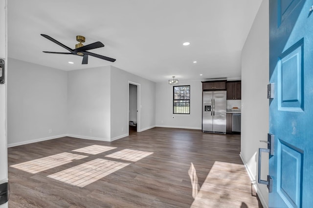 unfurnished living room featuring ceiling fan with notable chandelier and dark hardwood / wood-style flooring