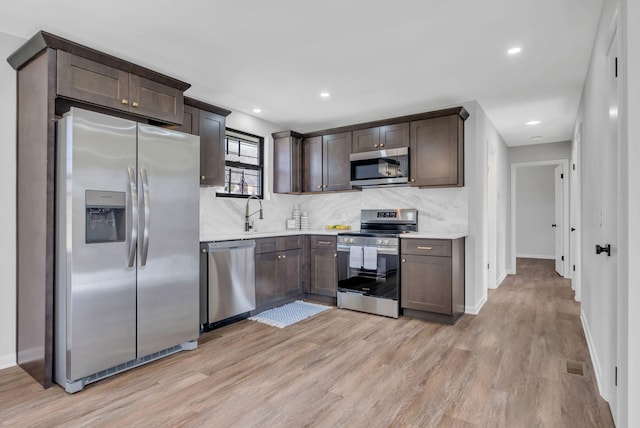 kitchen with appliances with stainless steel finishes, dark brown cabinetry, light hardwood / wood-style flooring, and sink