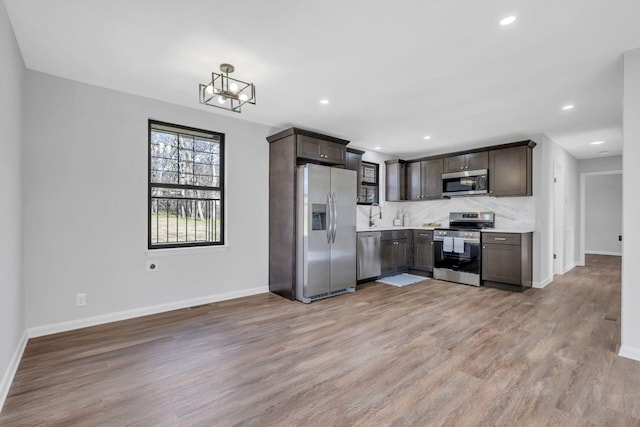 kitchen featuring sink, stainless steel appliances, backsplash, dark brown cabinets, and light wood-type flooring