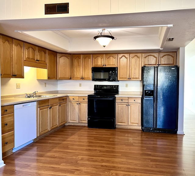 kitchen with sink, dark hardwood / wood-style flooring, a tray ceiling, black appliances, and ornamental molding