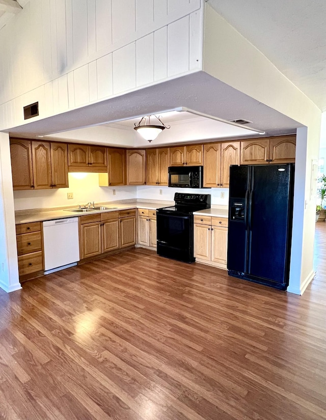 kitchen featuring dark wood-type flooring, black appliances, lofted ceiling, and sink