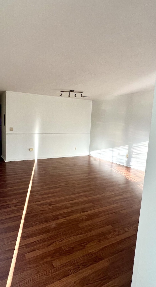 empty room with dark hardwood / wood-style flooring and rail lighting